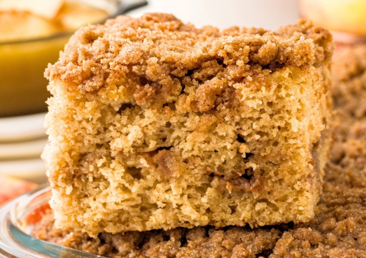 A close-up of a thick slice of crumb-topped coffee cake, showing its soft, moist interior and a generous, crumbly cinnamon topping.
