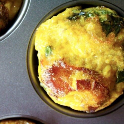 Close-up of a Breakfast Muffin in a muffin tin, showcasing its golden-brown top with visible pieces of spinach.