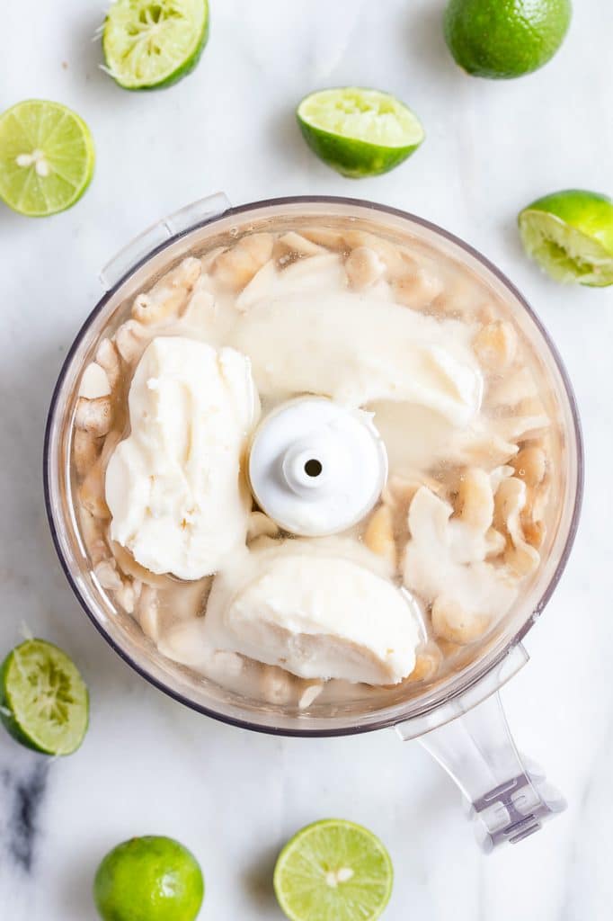 cashews, lime juice, and coconut butter in a food processor atop a marble kitchen counter