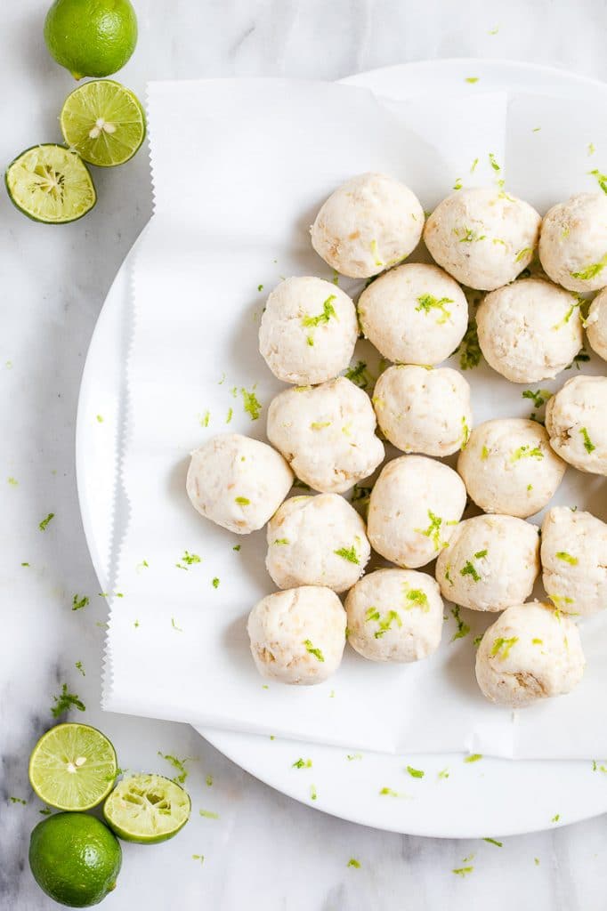 key lime pie fat bombs on a plate lined with a paper towel beside squeezed halved limes atop a marble kitchen counter