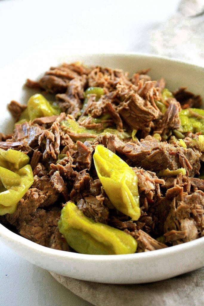 Low-FODMAP Pressure Cooker Italian Beef in a white ceramic bowl with lots of peperoncini