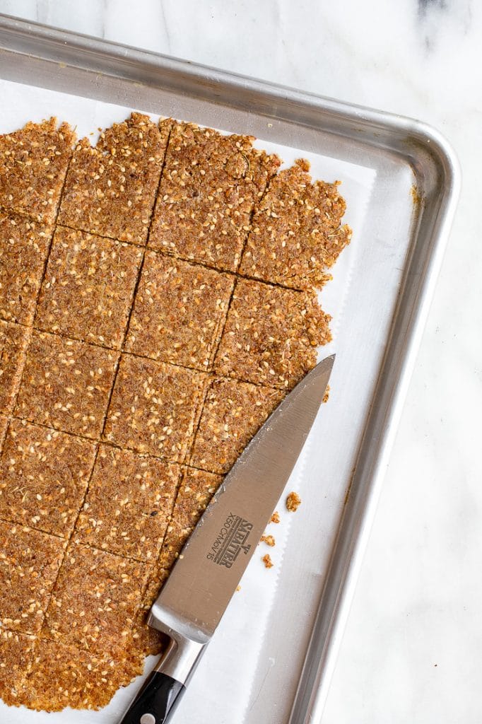 flattened low-carb crackers dough cut into squares with a knife on a baking tray lined with parchment paper