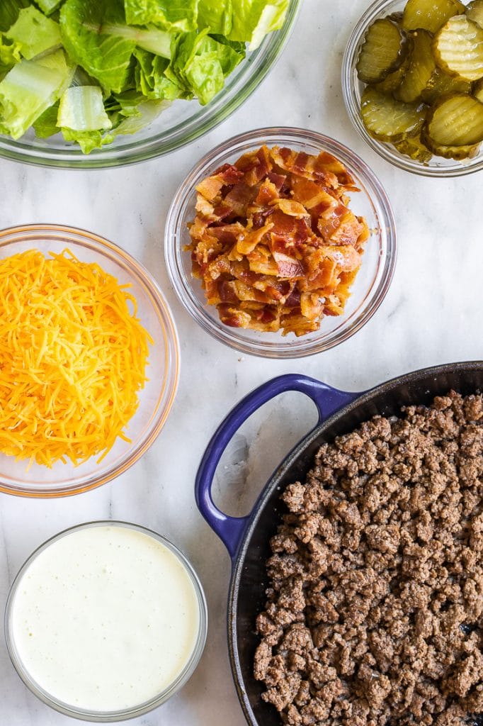 Keto Bacon Cheeseburger Salad ingredients assembled in separate bowls atop a marble kitchen counter