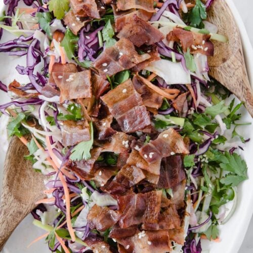 Keto bacon slaw on a serving plate with a wooden serving spoon.