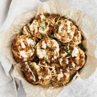 cheesy chicken fritters in a bowl lined with parchment paper with special sauce and chopped dill