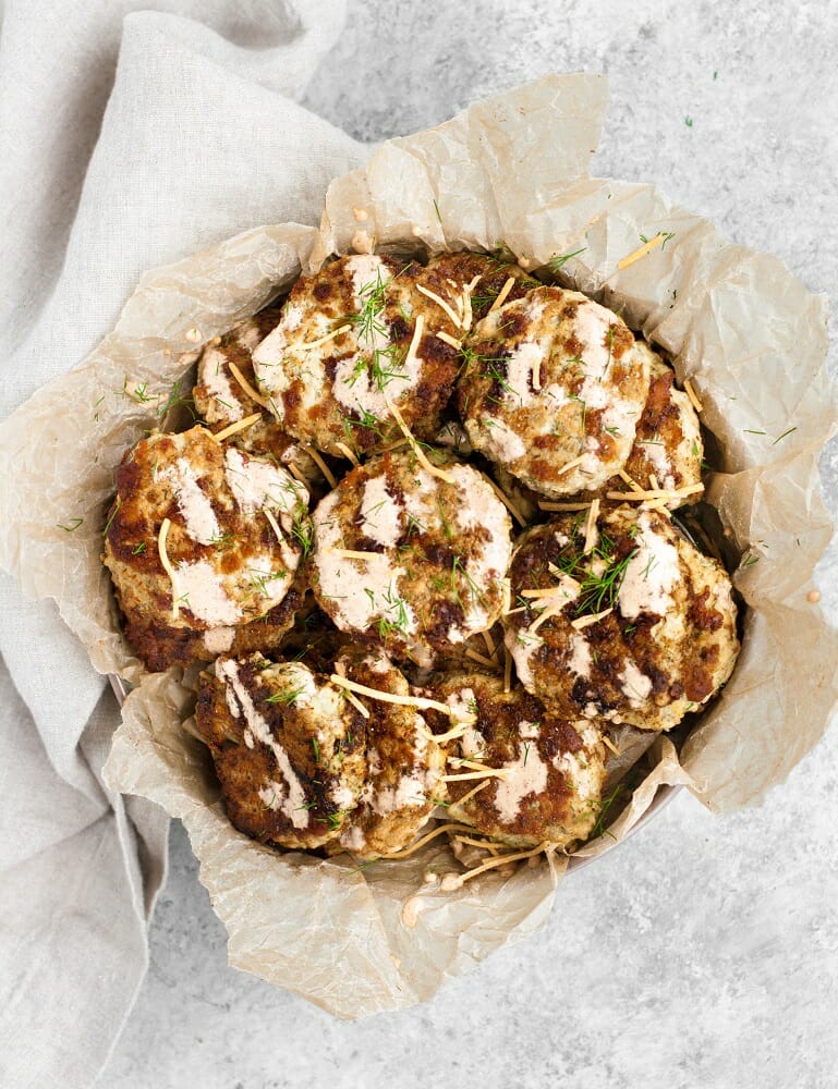 cheesy chicken fritters in a bowl lined with parchment paper with special sauce and chopped dill