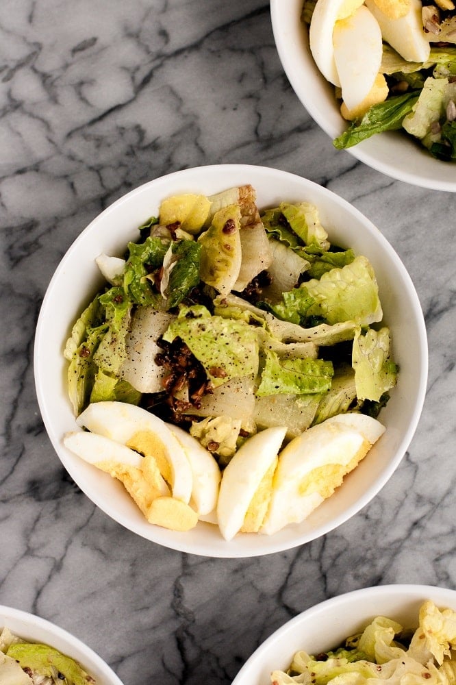 close-up-overhead-shot-of-bowl-of-warm-bacon-and-egg-salad-on-marble-board