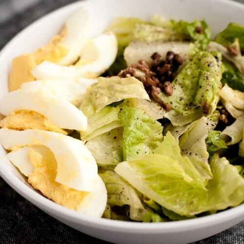 side-angle-shot-of-close-up-of-bowl-of-warm-bacon-and-egg-salad-on-marble-board