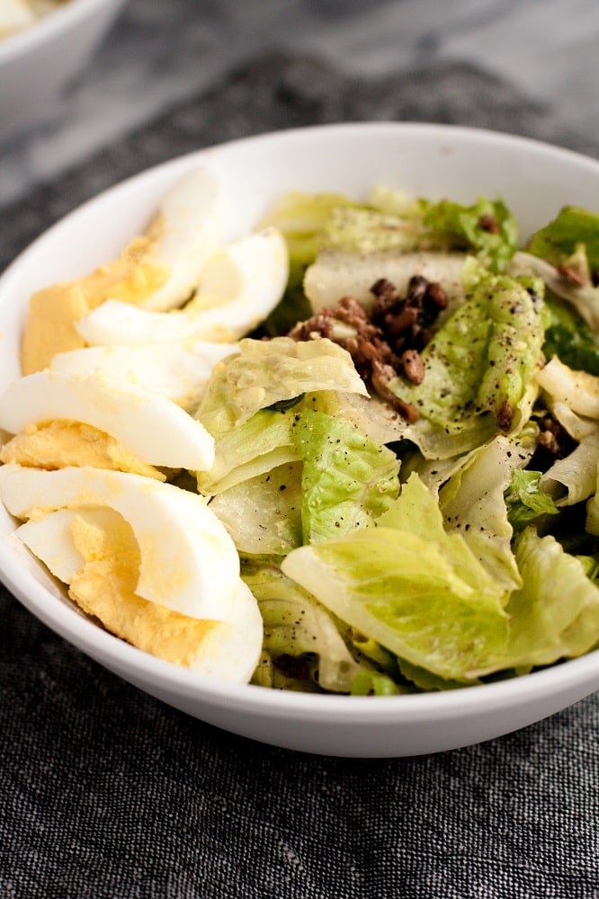 side-angle-shot-of-close-up-of-bowl-of-warm-bacon-and-egg-salad-on-marble-board