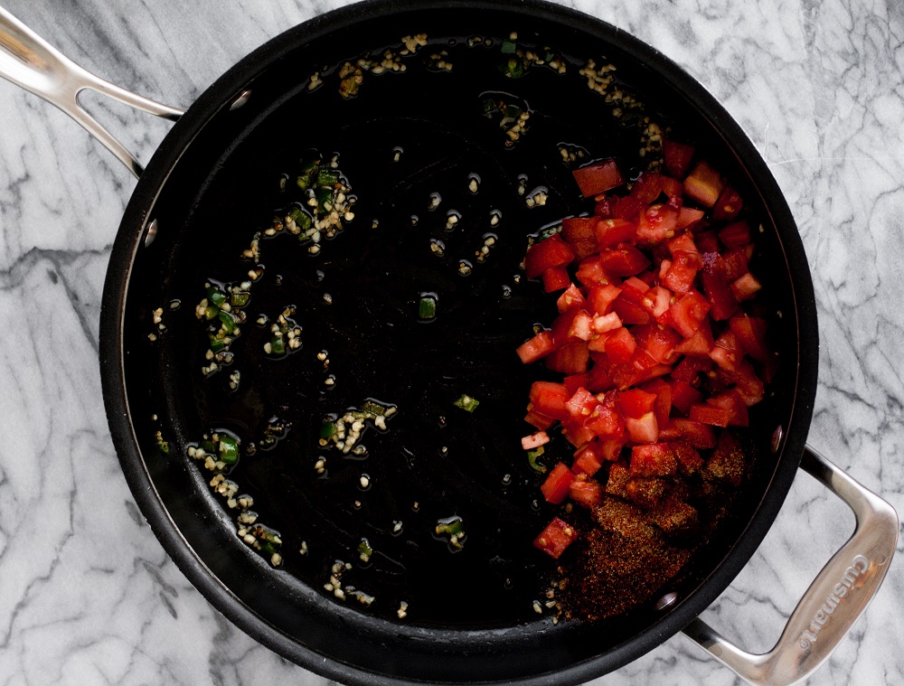 chopped-jalapenos-and-garlic-and-tomatoes-and-spices-in-black-pan-on-marble-board