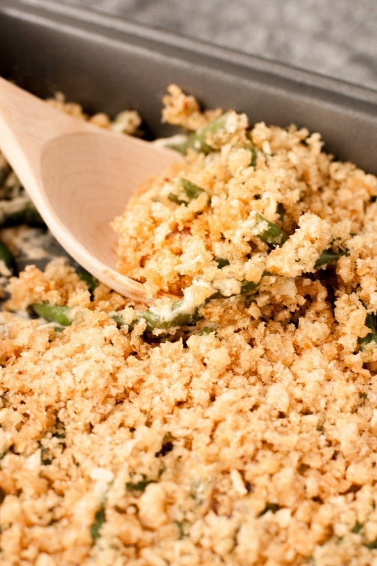 close-up-side-angle-bacon-green-bean-casserole-in-baking-pan-on-marble-board-with-wooden-spoon