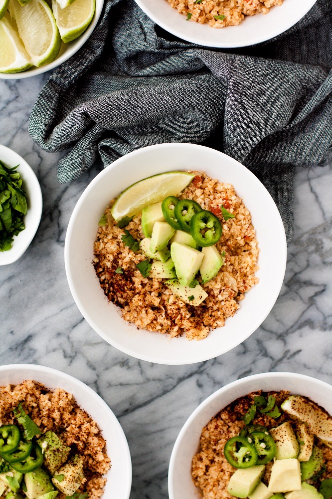 overhead-shot-of-mexican-cauliflower-rice-in-white-bowls-on-marble-board