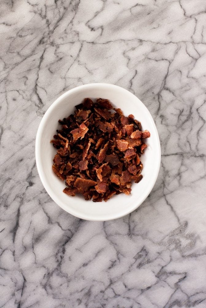 crumbled bacon in a small bowl atop a marble kitchen counter