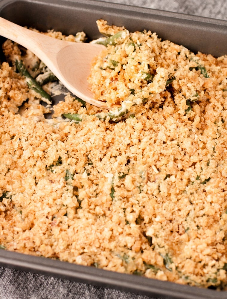 close-up-side-angle-bacon-green-bean-casserole-in-baking-pan-on-marble-board-with-wooden-spoon