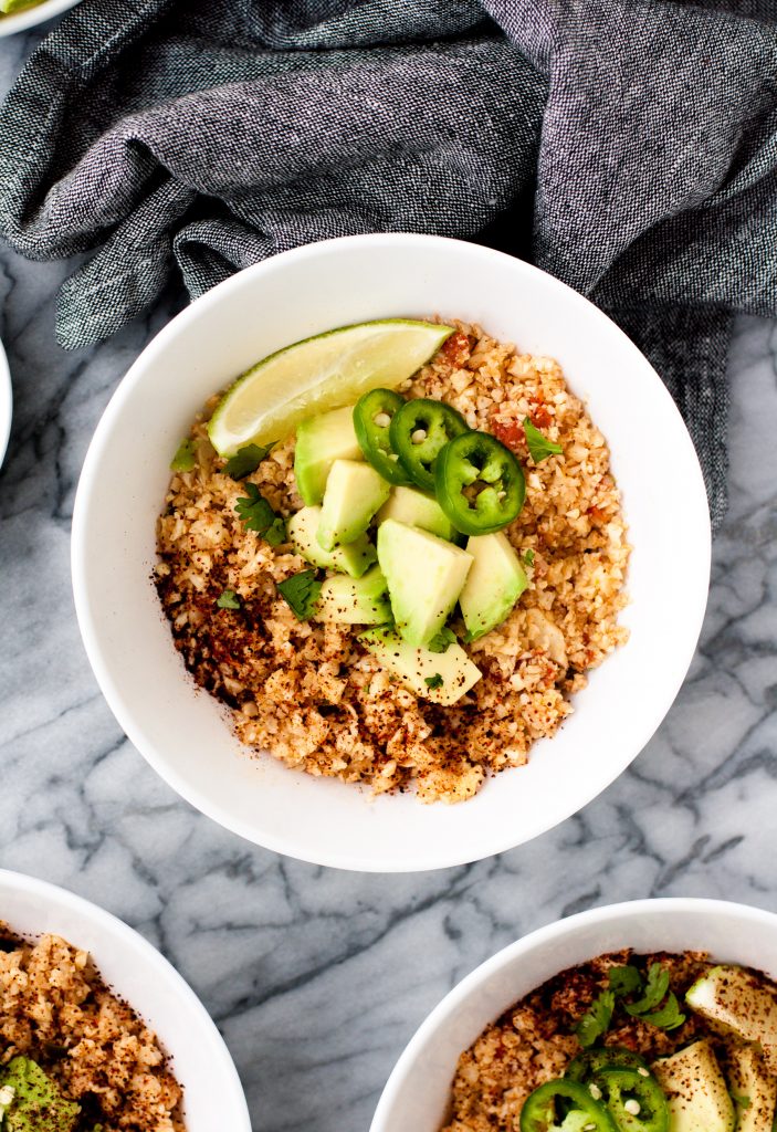 close-up-overhead-shot-of-mexican-cauliflower-rice-in-white-bowls-on-marble-board