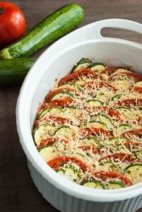 Keto Side Dish Recipes - parmesan zucchini tomato gratin in a baking dish beside fresh zucchinis and a tomato