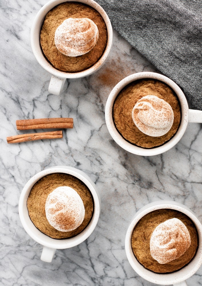 4 mugs of keto pumpkin pie mug cakes with whipped cream sprinkled with cinammon