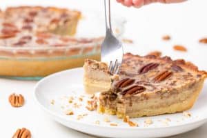 a serving of keto pecan pie on a fork with the rest of the pie in the background