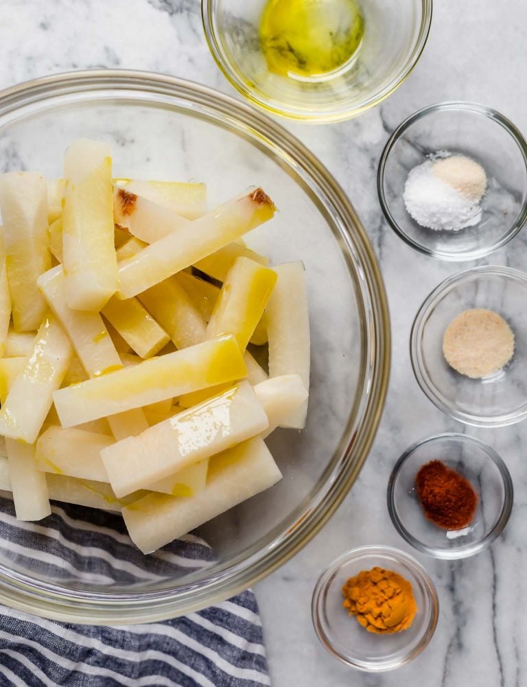 jicama fries in a large mixing bowl along with smaller bowls of spices avocado oil poured in