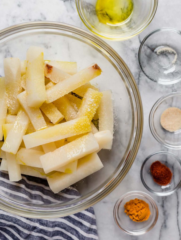 jicama fries in a large mixing bowl along with smaller bowls of spices salt and garlic powder poured in