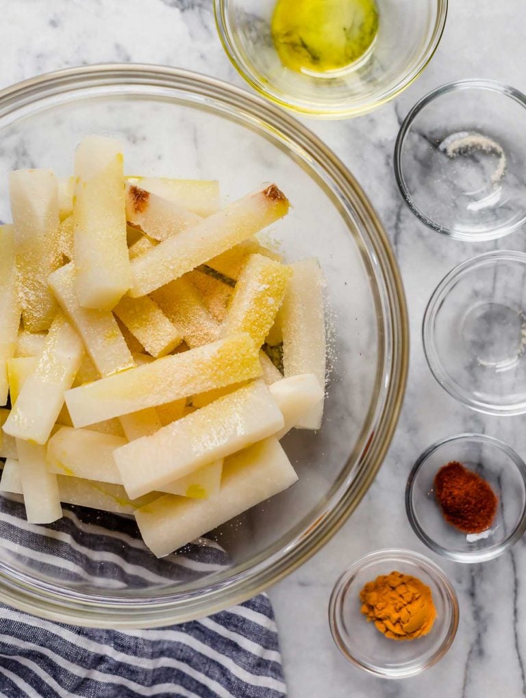 jicama fries in a large mixing bowl along with smaller bowls of spices onion powder poured in