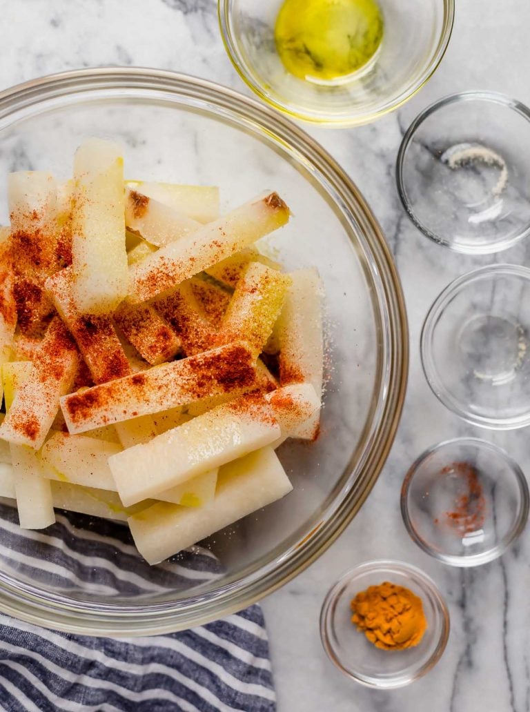 jicama fries in a large mixing bowl along with paprika and other spices poured in
