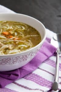 low carb keto chicken noodle soup i a bowl beside a spoon atop cloth table napkins