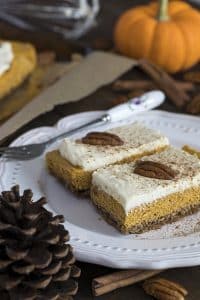 two servings of Low Carb & Sugar-Free Pumpkin Cheesecake Bars on a plate with a fork and fall decor