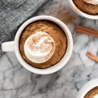 keto pumpkin pie mug cake with whipped cream and cinnamon on a marble table