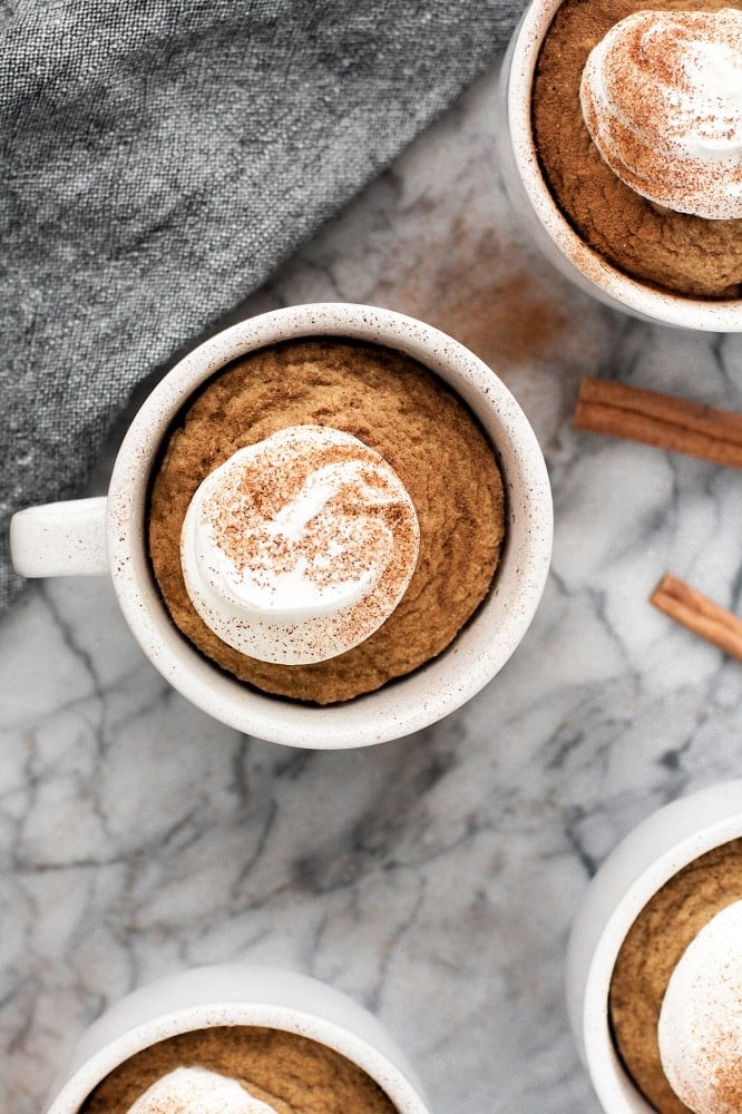 keto pumpkin pie mug cake with whipped cream and cinnamon on a marble table