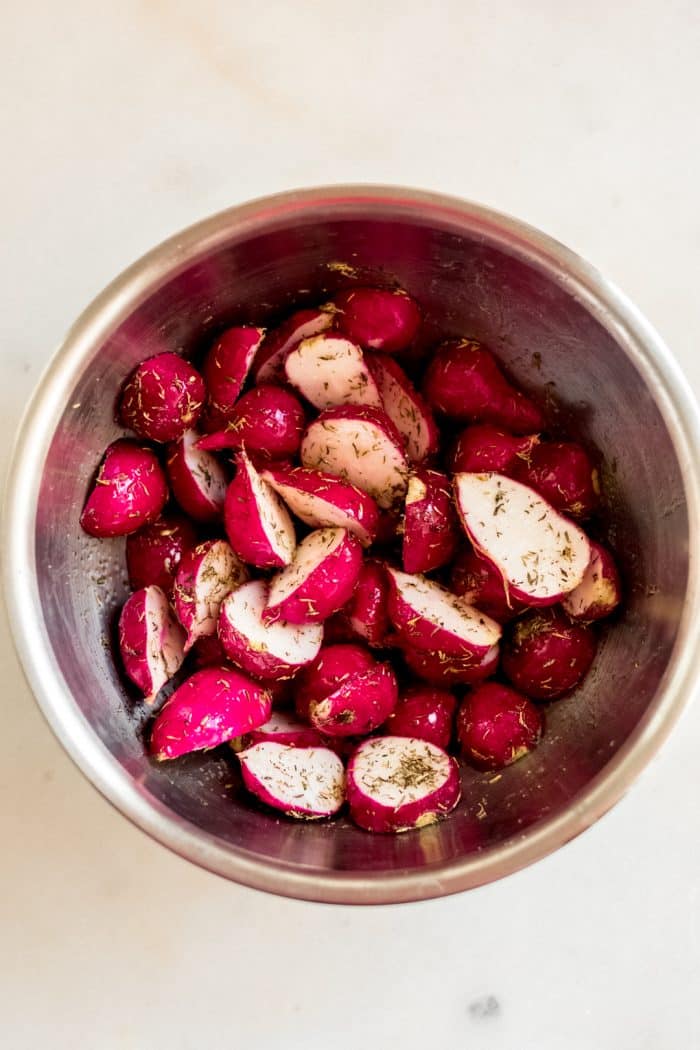 halved radishes in a stainless steel bowl dressed with oil and spices