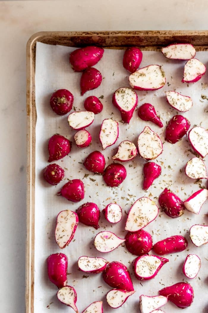radishes cut in half coated in oil and spices spread on a baking sheet