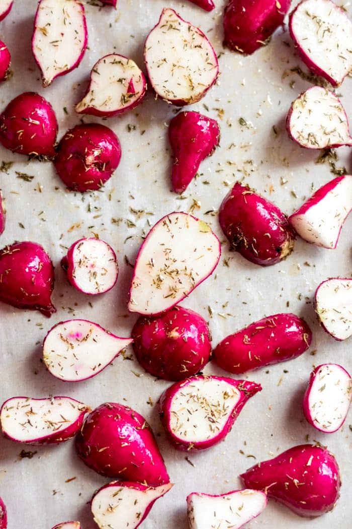 radishes cut in half coated in oil and spices spread on a baking sheet
