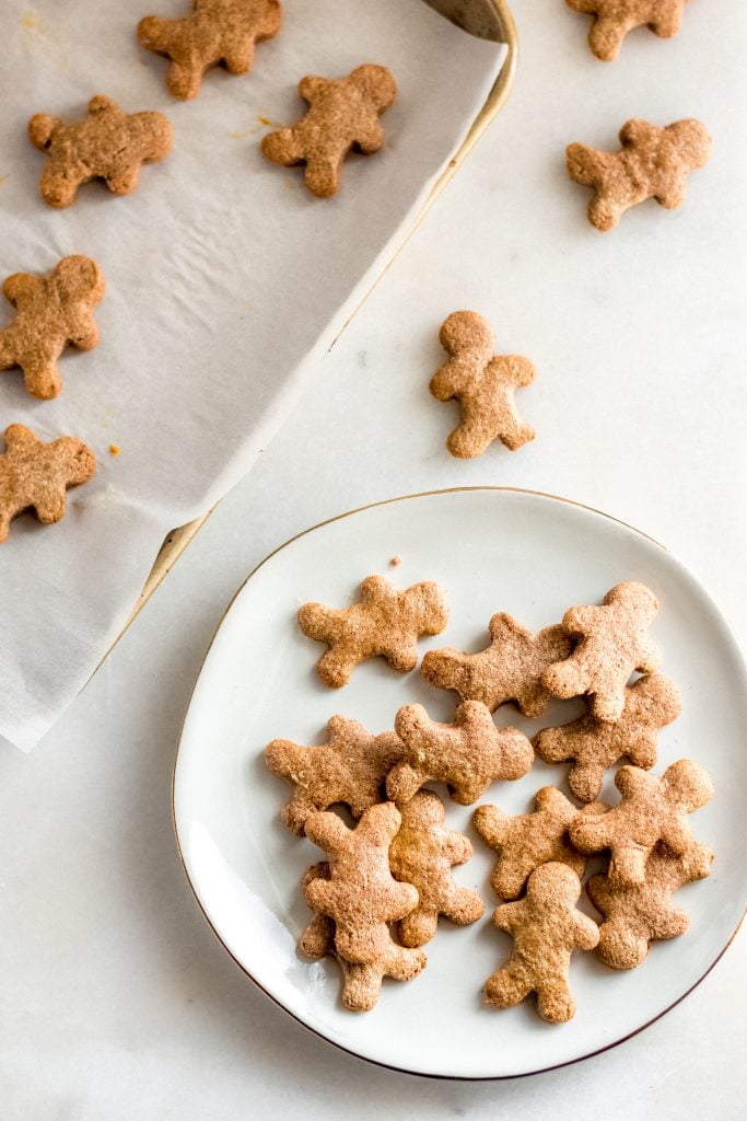 keto gingerbread cookies transferred onto a white ceramic saucer beside baking sheet lined with parchment paper atop a marble counter