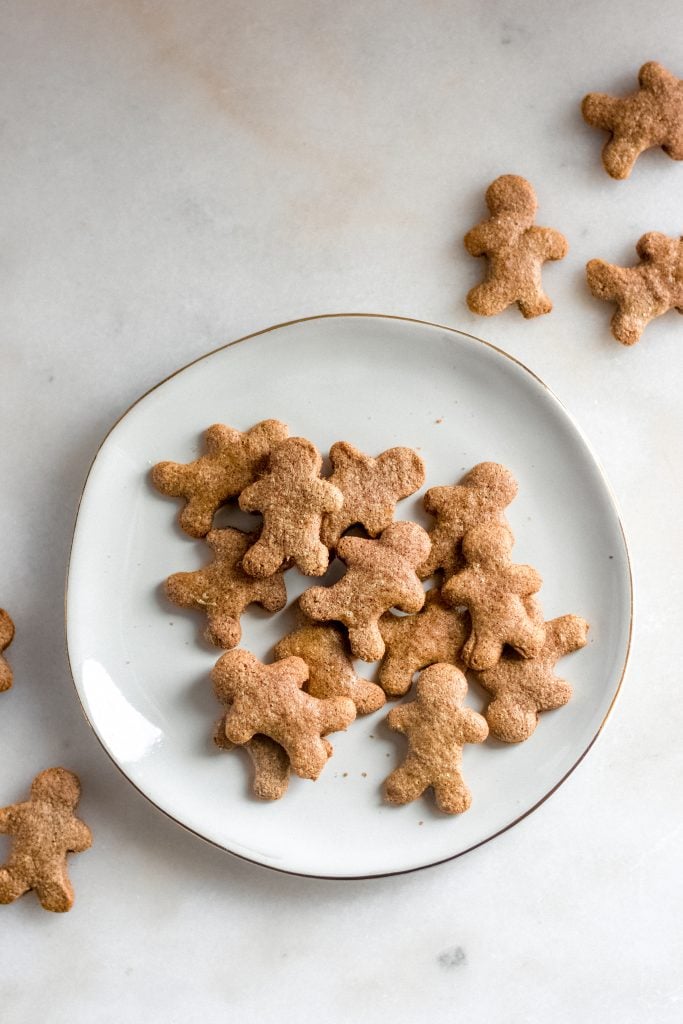 13 keto gingerbread cookies on a ceramic saucer on top of a marble counter with gingerbread-men scattered around
