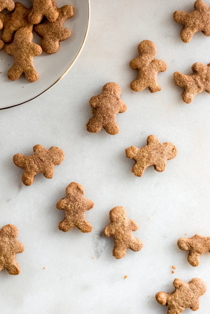 keto gingerbread cookies spread across a marble counter some on a white ceramic saucer