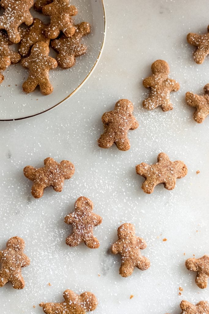 keto gingerbread cookies spread across a marble counter some on a white ceramic saucer dusted with lakanto sweetener
