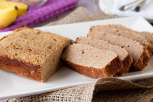 Sliced Grain-free Banana Bread on a white tray with bananas in the background