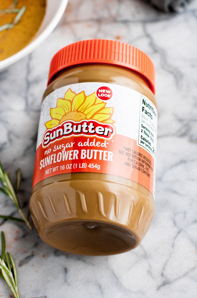 SunButter jar of no-sugar-added sunflower butter on top of a marble kitchen counter beside rosemary sprigs