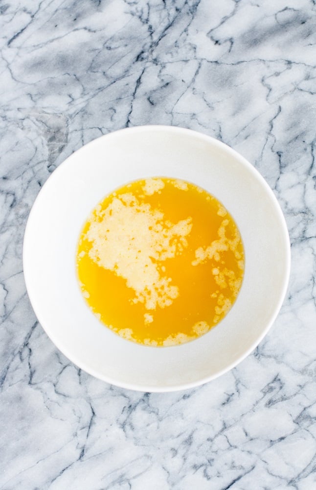 melted butter in a white microwave-safe bowl on top of a marble counter