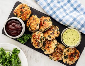 kale and mushroom sausage patties on a rectangular wooden board with 2 dip variants