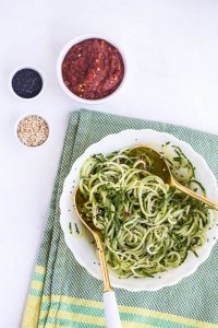 Bowl of Sesame Marinated Cucumber Noodles with copper spoons and bowls of spices