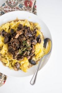 Bowl of Spaghetti squash with roasted mushrooms and garlic sauce on a patterned cloth