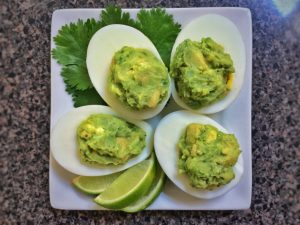 4 guacamole deviled eggs with lime and cilantro on a square plate