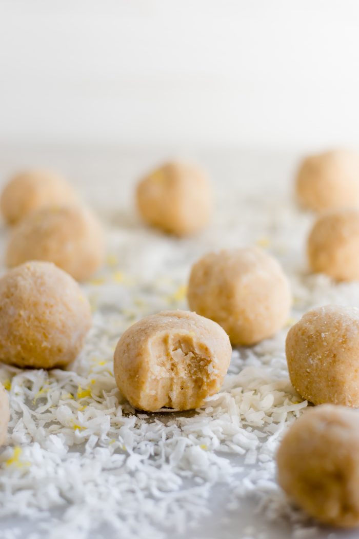 ten lemon bar fat bombs with one having a tiny bite mark on a bed of desiccated coconut