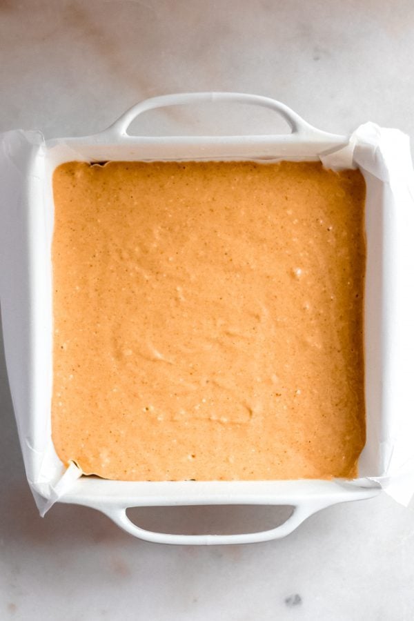 pumpkin cheesecake batter poured into a square baking pan lined with parchment paper