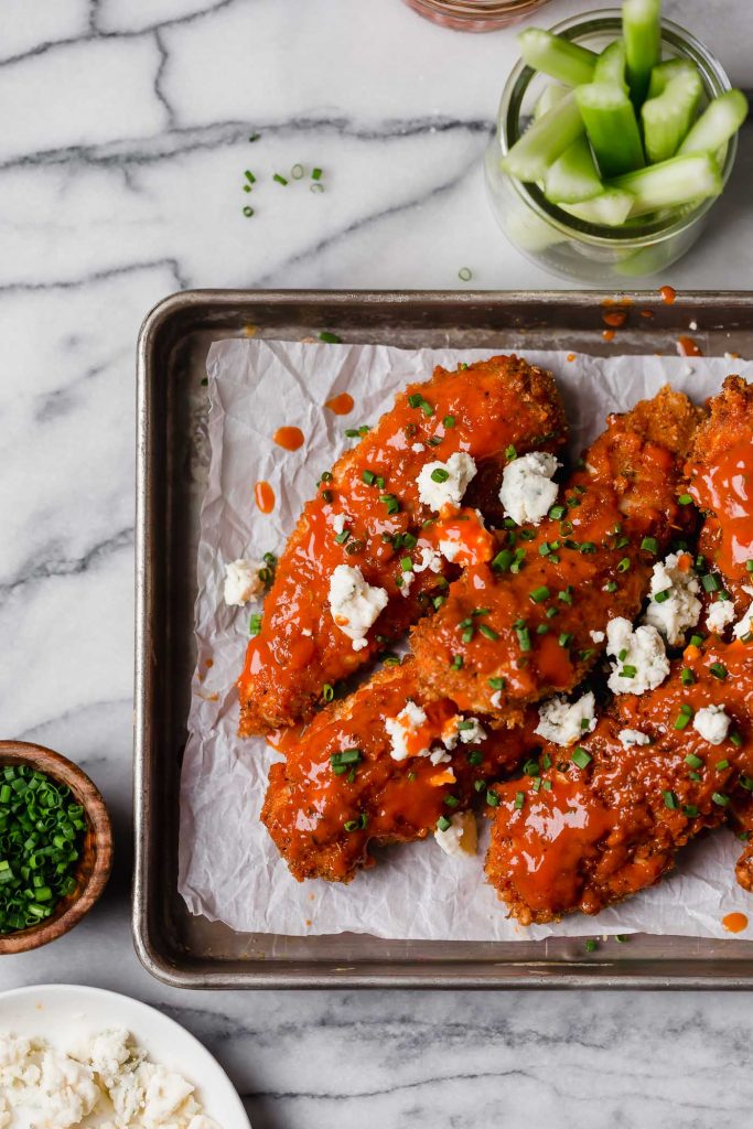baked chicken tenders with buffalo sauce crumbled blue cheese and chopped chives on a baking pan