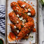 overhead hero image buffalo chicken tenders on a baking pan with spoon on top of a marble counter