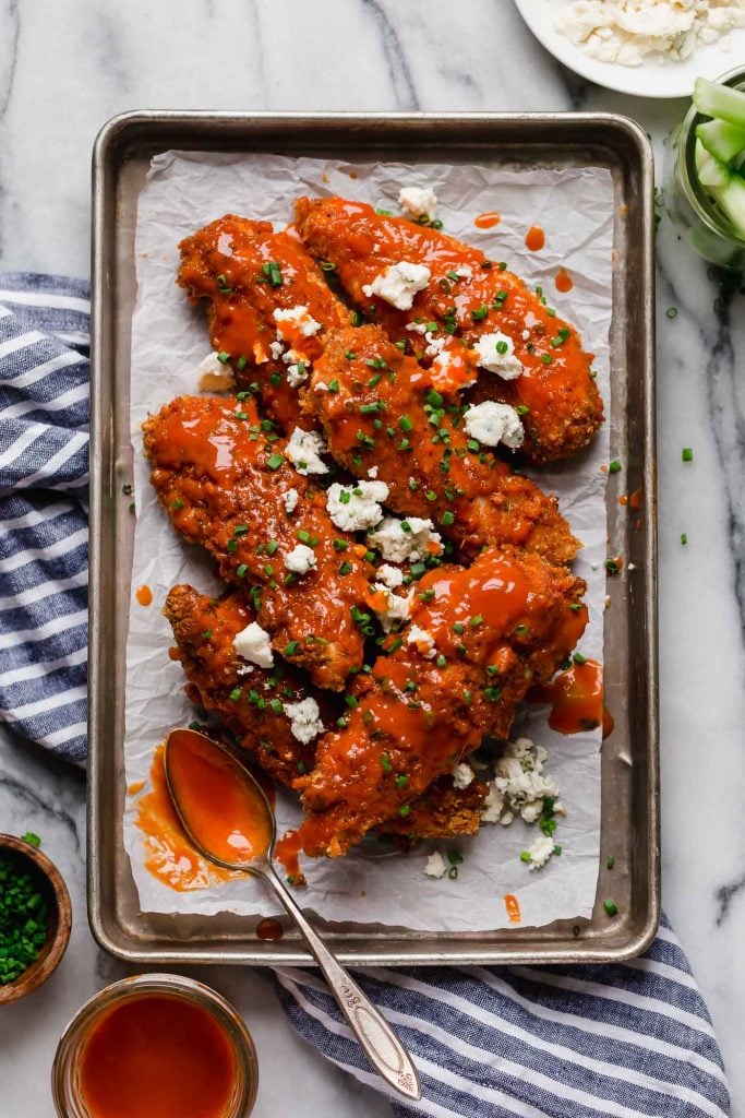 overhead hero image buffalo chicken tenders on a baking pan with spoon on top of a marble counter