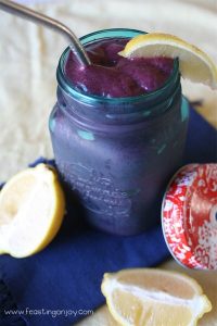 Ginger, Lemon, Blueberry Detox Smoothie in a blue glass mason jar with a stainless steel straw beside lemon wedges